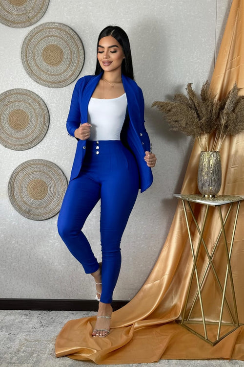 Mujer con traje azul rey y top blanco, fondo elegante con adornos de mimbre y cortina dorada