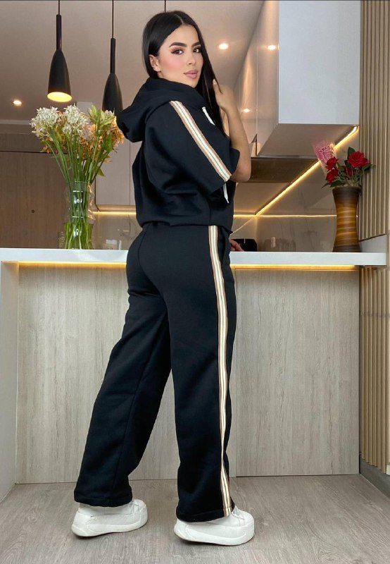 Mujer con conjunto deportivo negro de sudadera y pantalón con franjas beige, en cocina moderna.